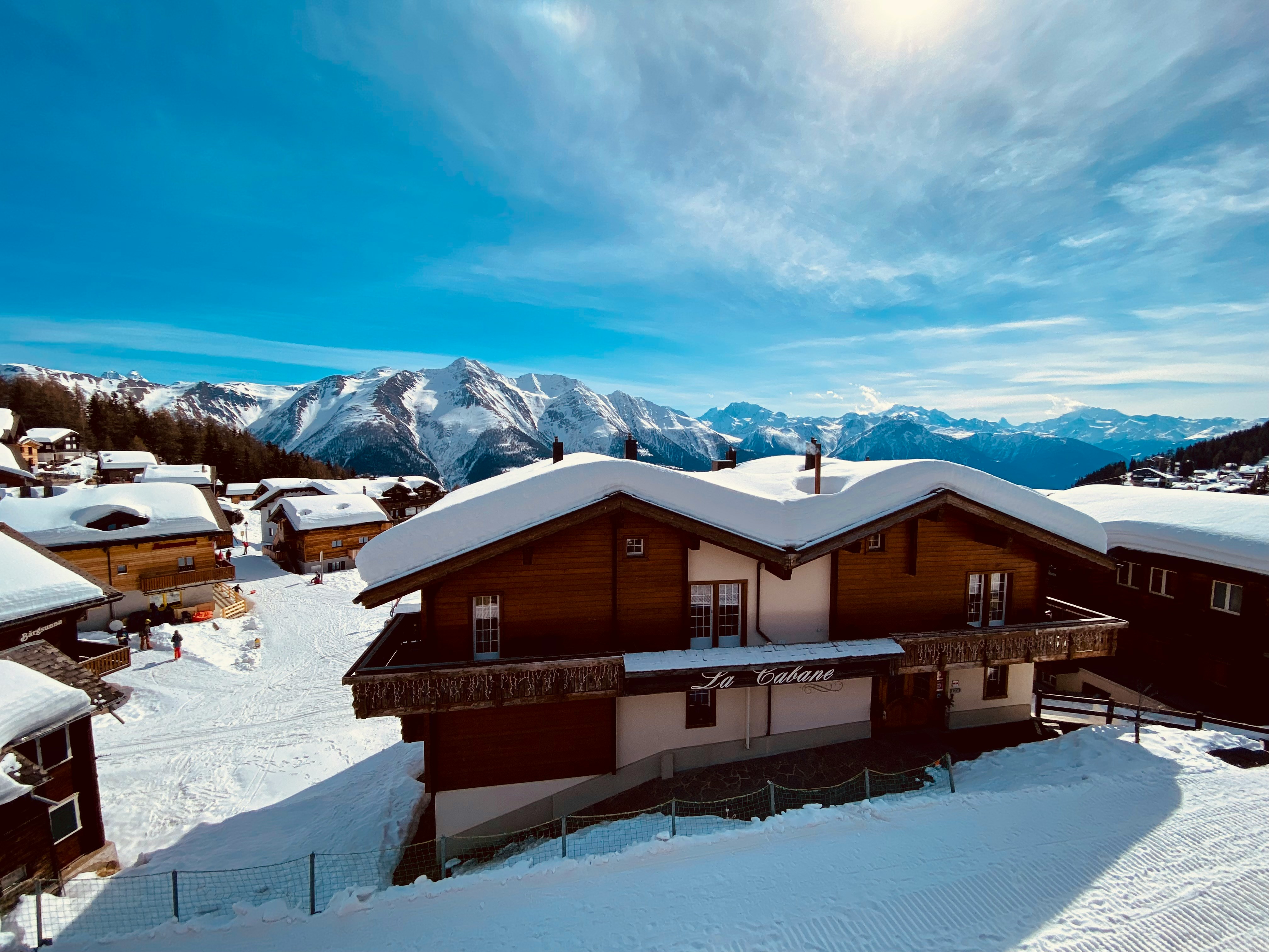 Snow-covered mountain chalet with ski runs behind it